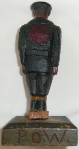 Item 455 View 3 of 4 Wooden carving of a PoW in navy coat seen from the back. Large red circle on back of jacket 